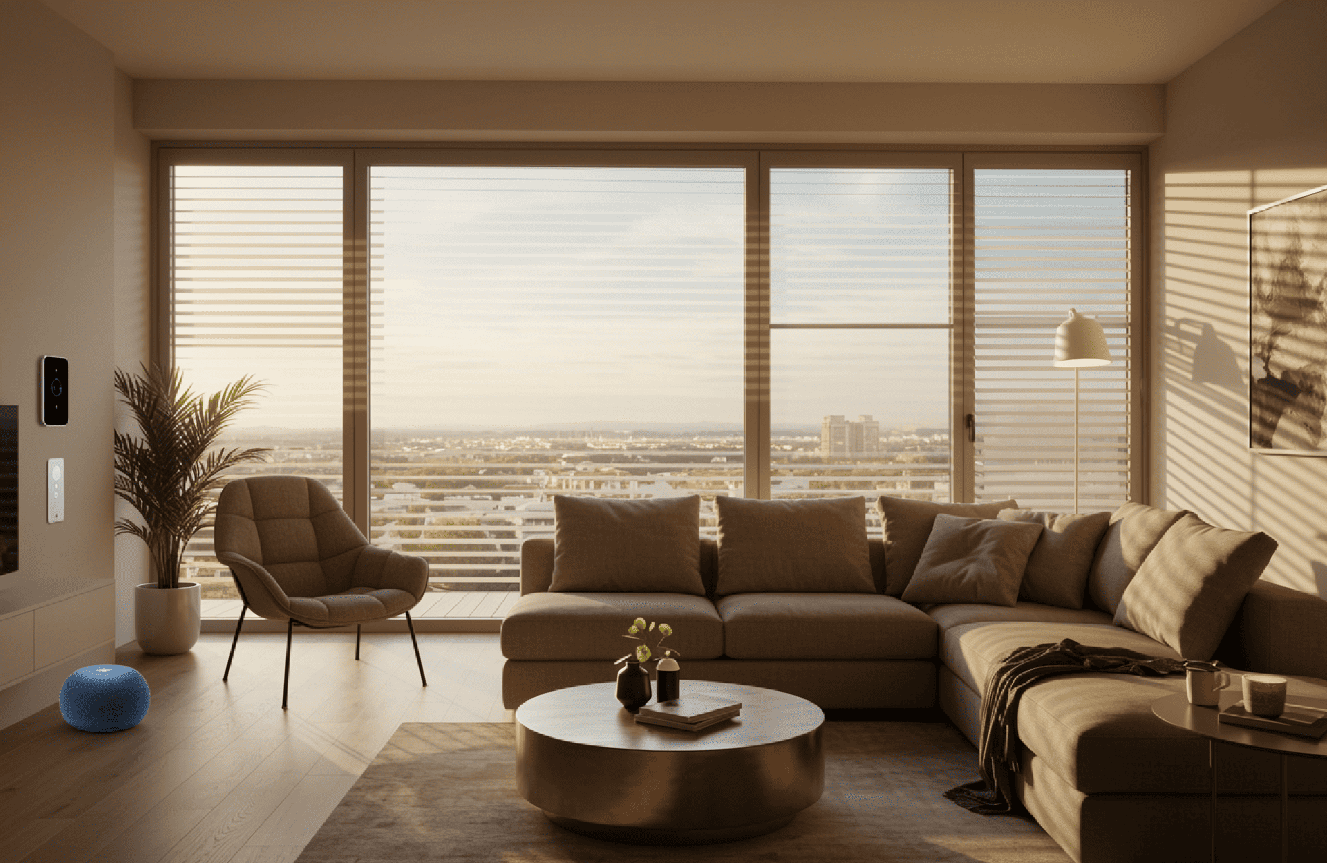 Symmetry Shading Modern living room with large windows, a sectional sofa, armchair, round coffee table, houseplant, wall-mounted devices, and a blue smart speaker, overlooking a cityscape at sunset. Shading & Automation Specialists